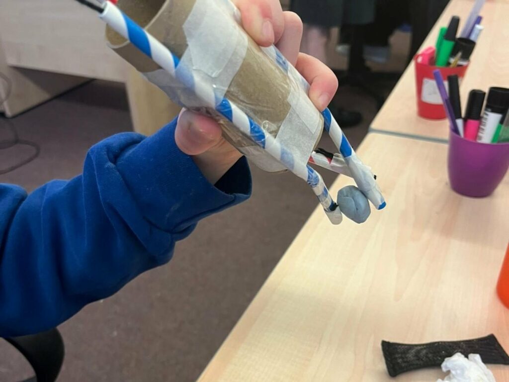 A child holds up a paper and straw rocket they have just built